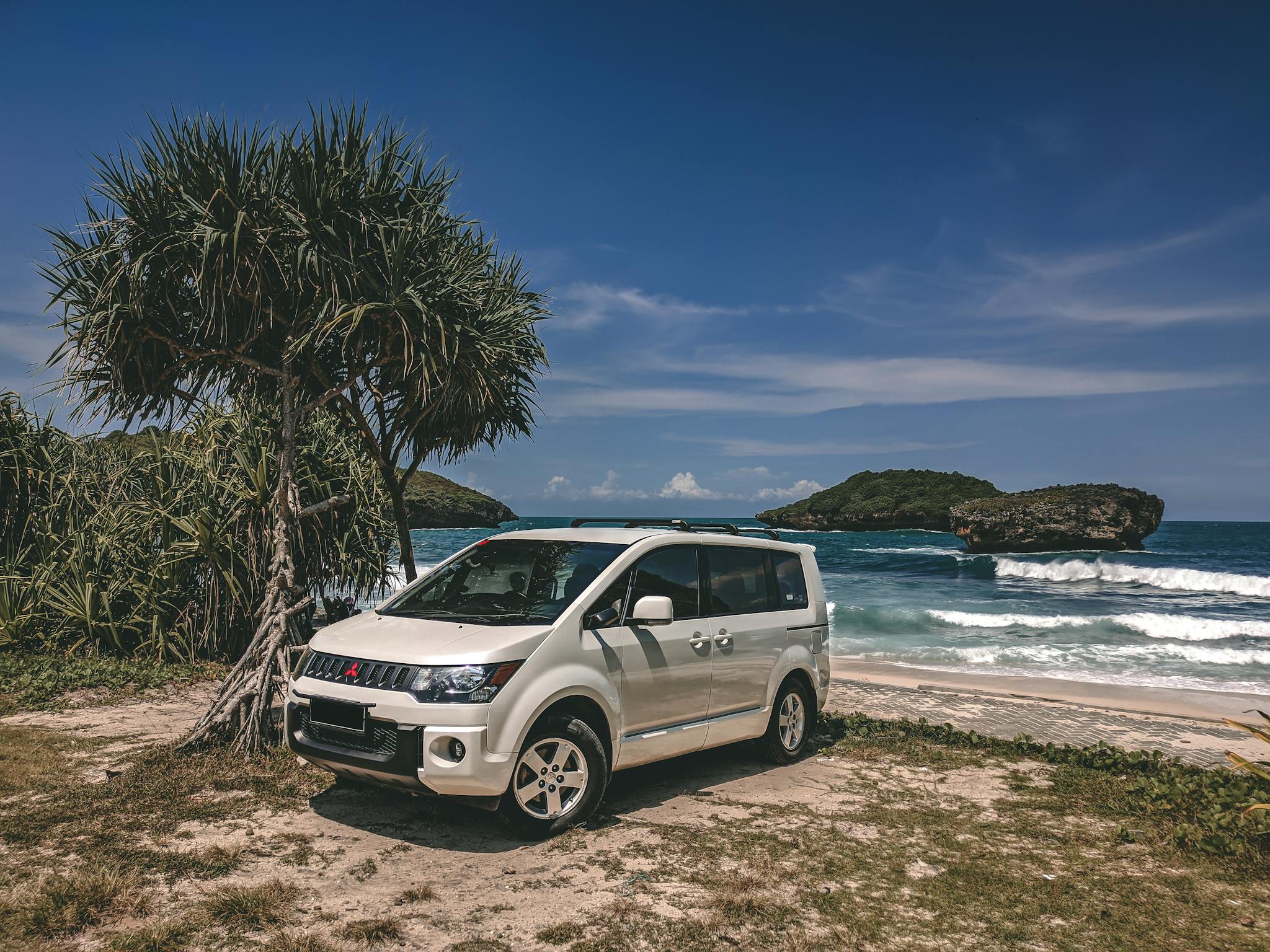A white SUV parked on a scenic beach in Pacitan, Indonesia, with clear blue sky and ocean waves.