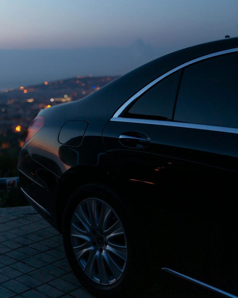 Sleek luxury black car parked at dusk, with city lights in background creating an elegant silhouette.